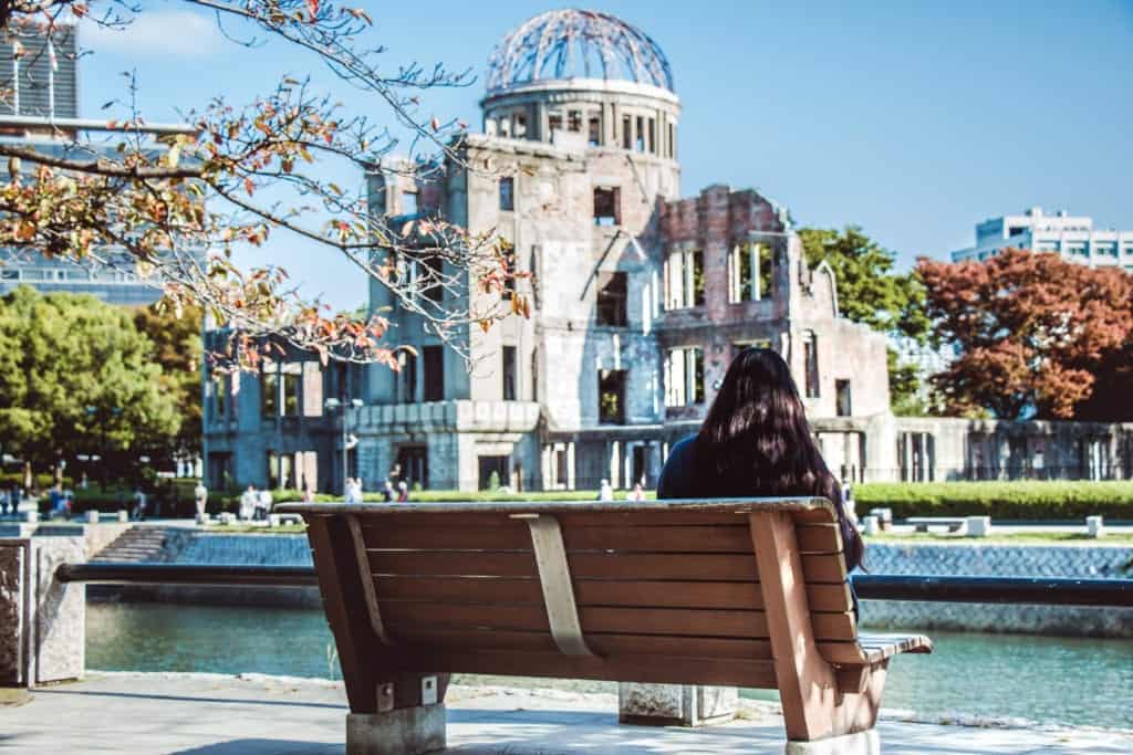 Girl sit on the bench, look at Atomic Dome from Hiroshima Peace Memorial park in the autumn season of Hiroshima, Japan.