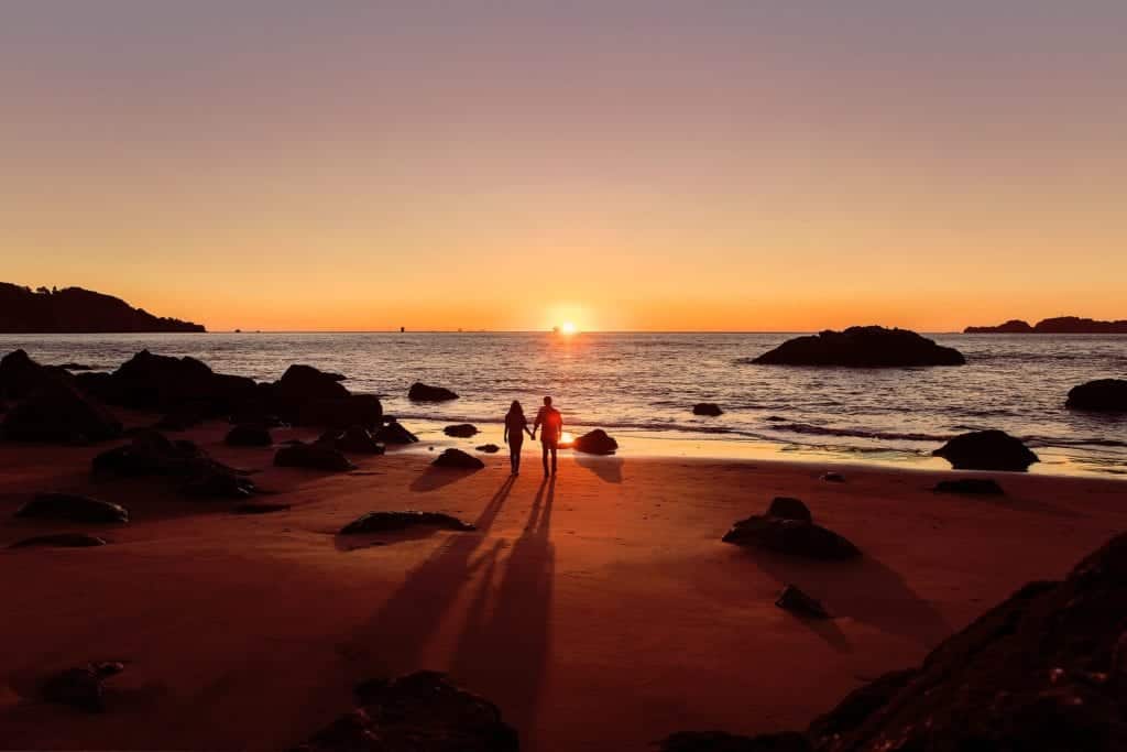 Par promenerar mot havet i solnedgång.