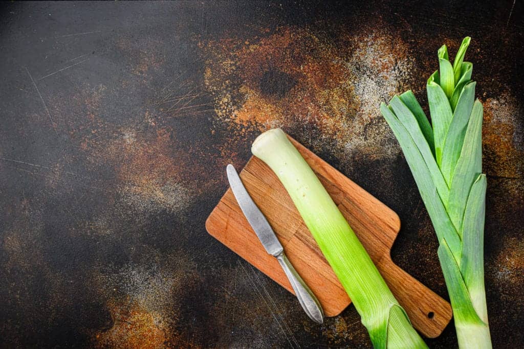Organic leek stalks with herbs ingredients for cooking Braised Leeks, onrustic metall background dark, top view with space for text
