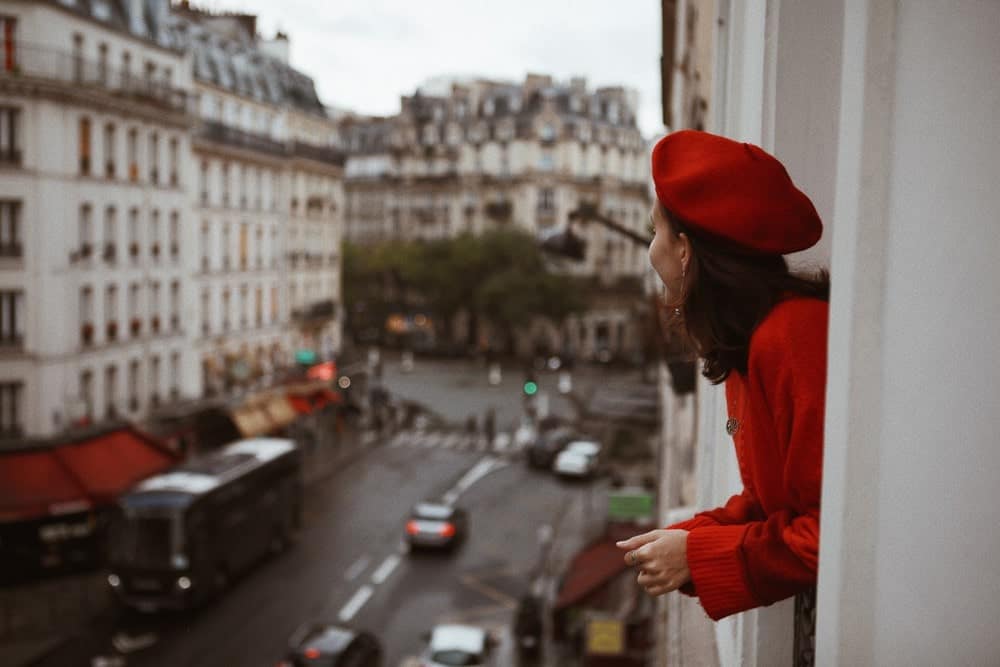 Kvinna tittar ut ur sitt fönster i röd basker.